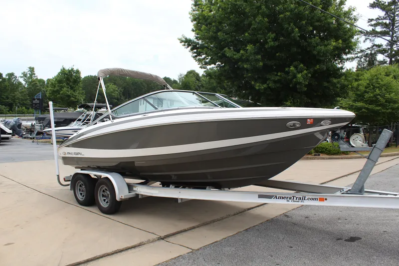 Slide: The Image of 2011 Regal 2100 boat on trailer, parked outdoors with trees in the background. - 8