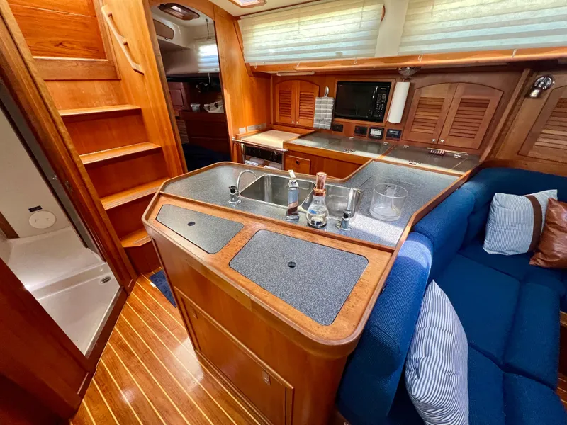 Slide: The Image of 1999 Sabre 402 yacht interior with wooden cabinetry, kitchen sink, and blue seating. - 14