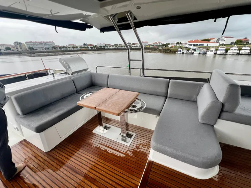 Slide: The Image of Beneteau Swift Trawler 54 (2025) deck with gray seating and wooden table by the water. - 27