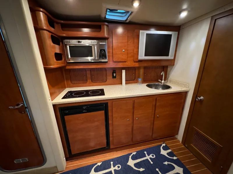 Slide: The Image of 2008 Rinker 370 yacht kitchen with microwave, stove, sink, and wooden cabinetry. - 21