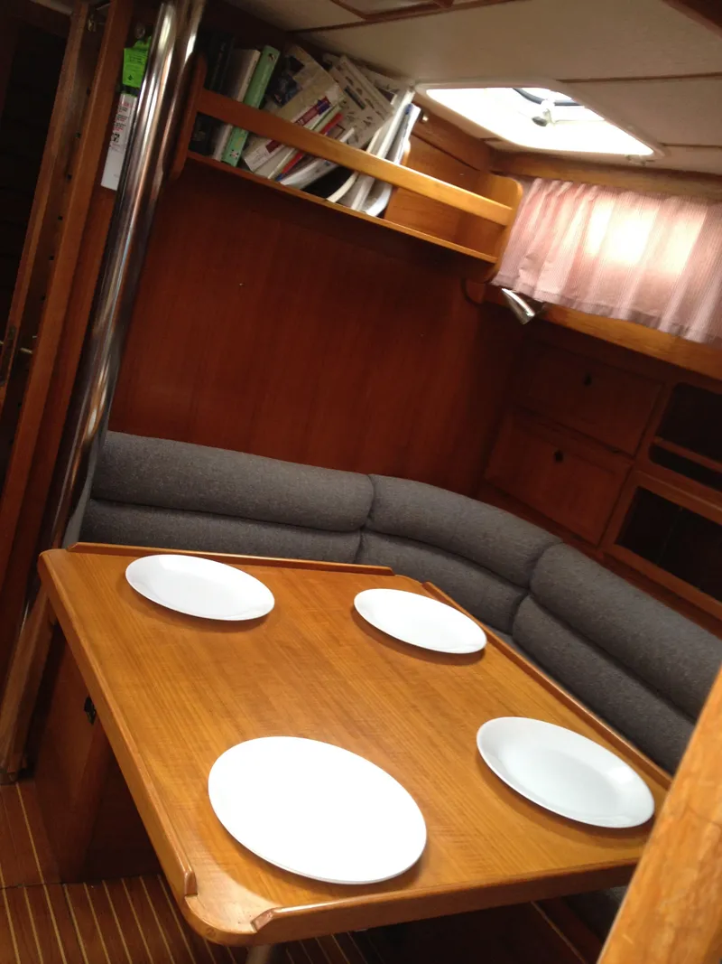 Slide: The Image of Cozy dining area in a 1985 Nauticat 38 sailboat with wooden table and cushioned seating. - 38