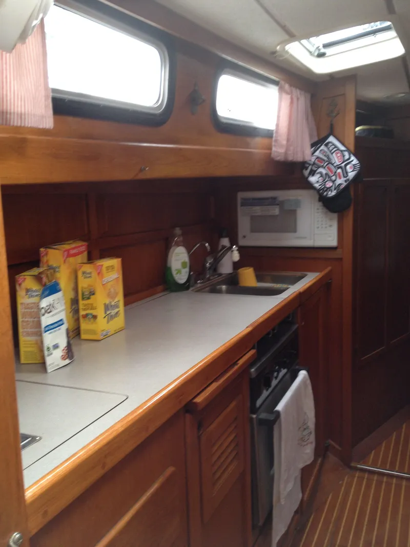 Slide: The Image of 1985 Nauticat 38 sailboat galley with wooden cabinetry, microwave, and countertop essentials. - 39