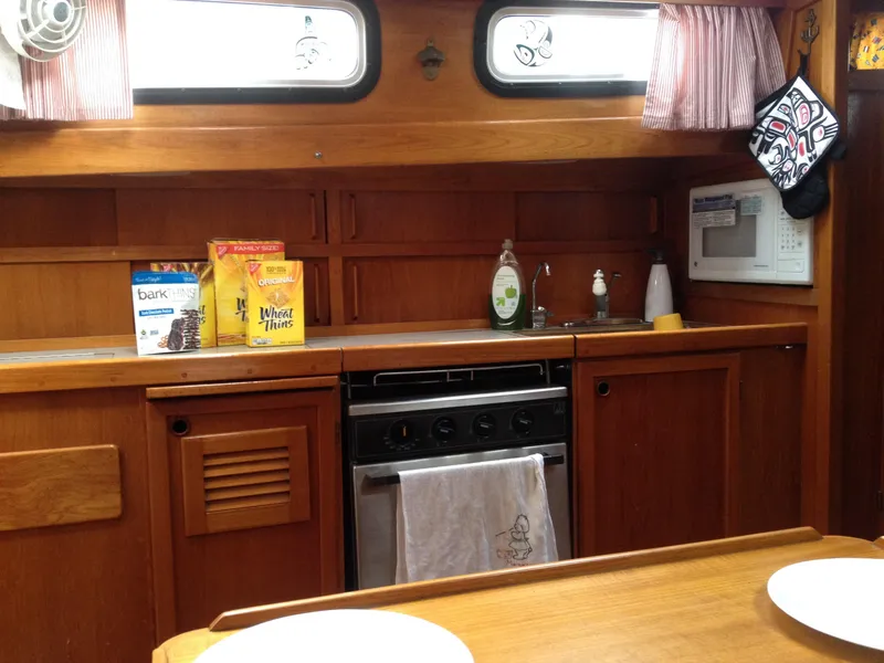 Slide: The Image of 1985 Nauticat 38 sailboat kitchen with wooden cabinets, stove, microwave, and snacks on the counter. - 41