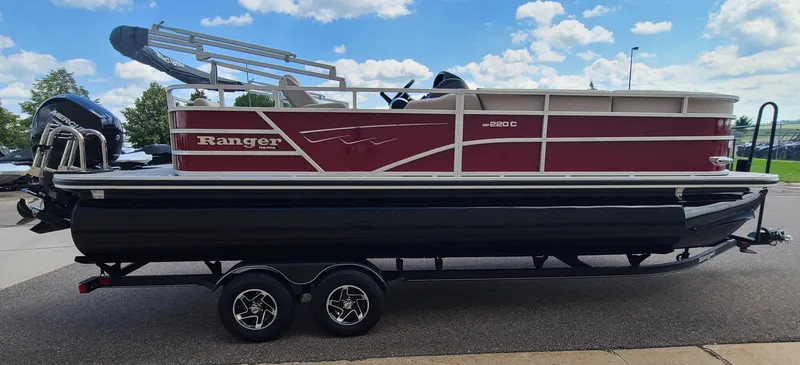 The Image of 2024 Ranger Reata 220C pontoon boat on trailer, parked outdoors under a blue sky. - 0