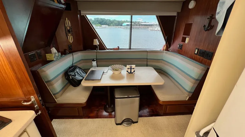 Slide: The Image of 1987 Hatteras Motoryacht interior with cozy dining area, striped seating, and waterfront view. - 28