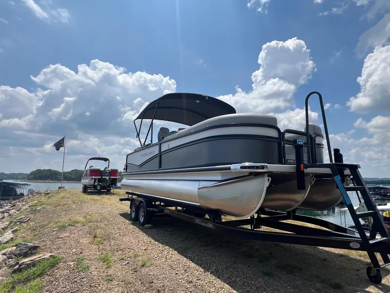 Slide: The Image of 2024 Premier 230 Sunsation RE pontoon boat on trailer by lake. - 2
