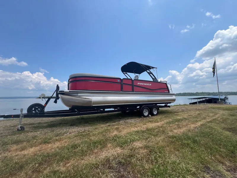Slide: The Image of 2024 Premier 250 SunSation RF pontoon boat on trailer by a lake. - 3