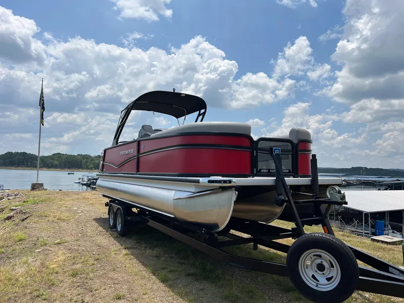 Slide: The Image of 2024 Premier 250 SunSation RF pontoon boat on trailer by a lake. - 4