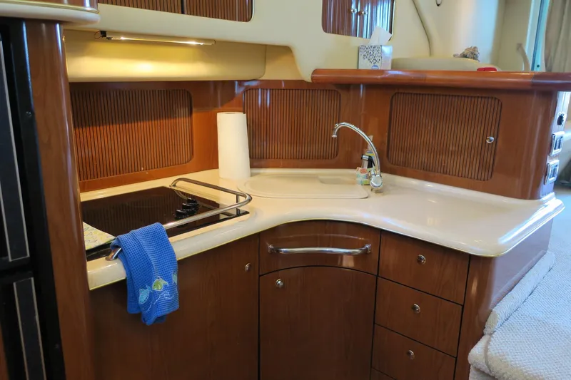 Slide: The Image of 2002 Sea Ray 400 Sedan Bridge kitchen with stove, sink, and wooden cabinetry. - 42