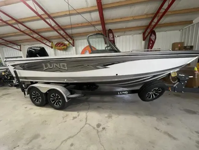 Slide: The Image of 2025 Lund 1975 Tyee boat in showroom, featuring sleek design and dual-axle trailer. - 1