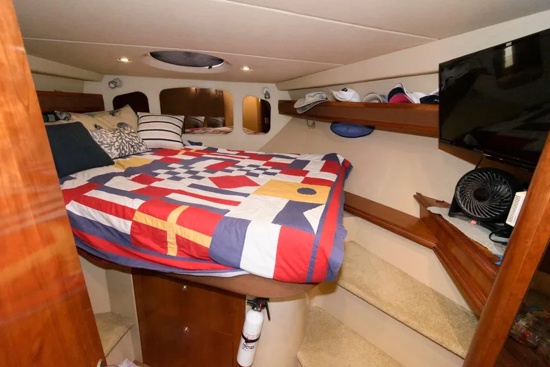 Slide: The Image of 2004 Cruisers Yachts 370 Express cabin with colorful bedspread, TV, and storage shelves. - 12