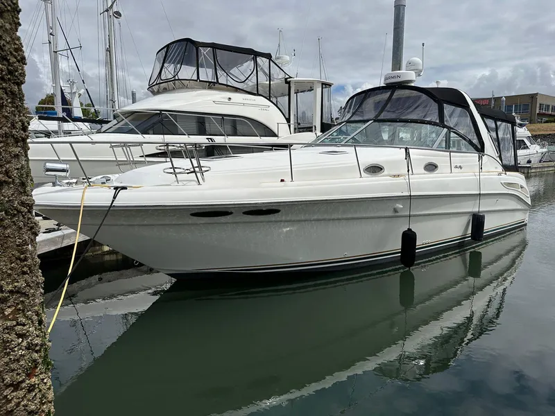 Slide: The Image of 1999 Sea Ray 340 Sundancer boat docked in marina, featuring sleek white design and black canopy. - 0