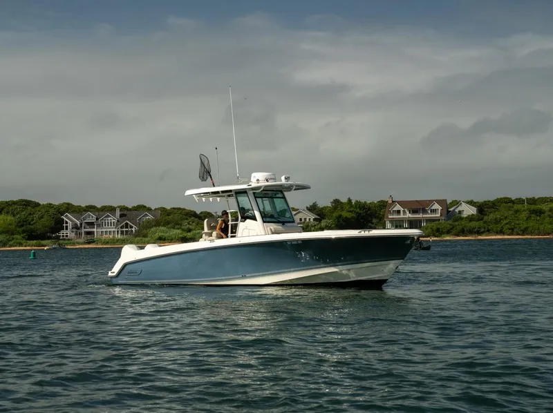 Slide: The Image of 2022 Boston Whaler 330 Outrage boat cruising on a calm lake near shoreline homes. - 4