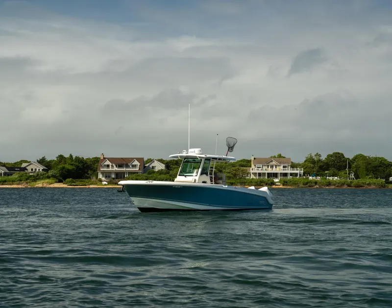 Slide: The Image of 2022 Boston Whaler 330 Outrage boat cruising near coastal homes under cloudy skies. - 7