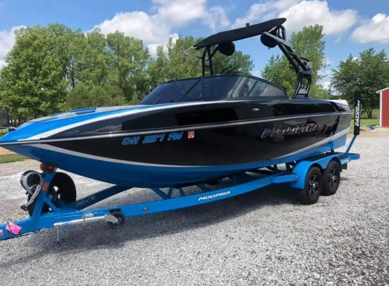Slide: The Image of 2019 Moomba Craz boat on a blue trailer, parked on gravel with trees in the background. - 4
