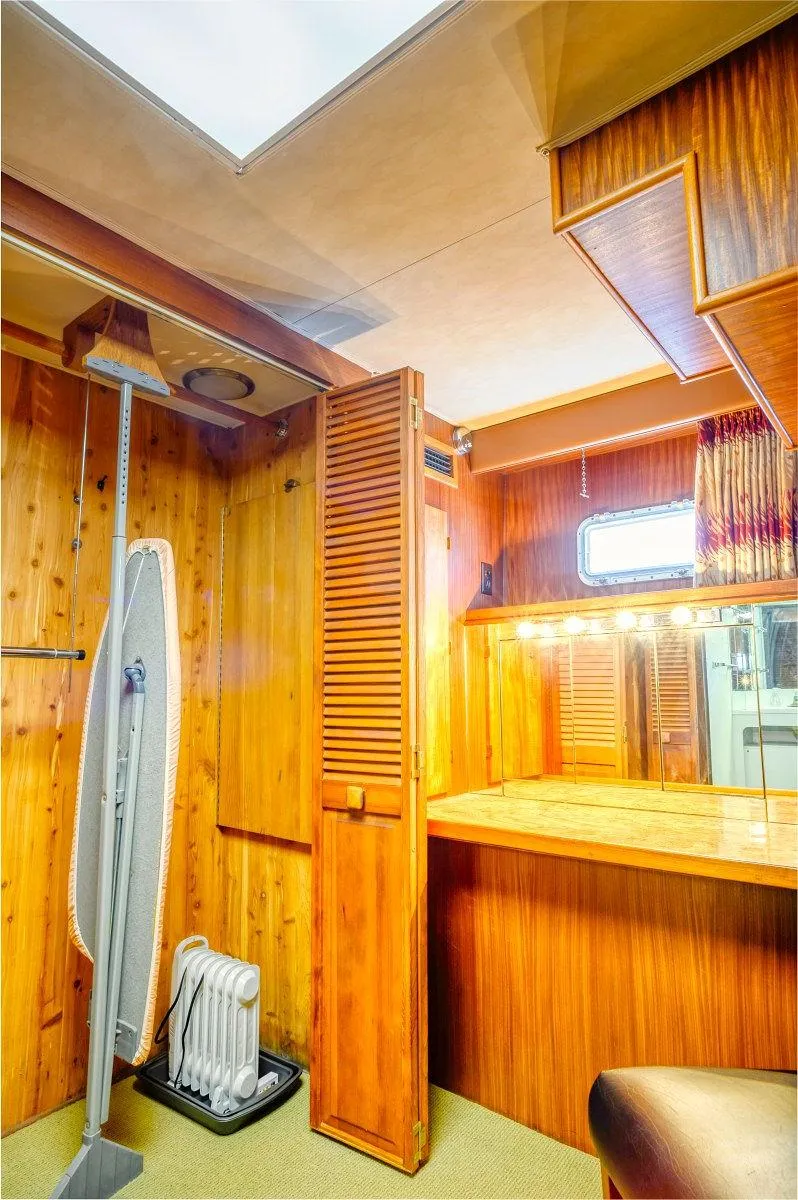 Slide: The Image of 1987 Hatteras 72 Yacht interior with wooden paneling, ironing board, and vanity area. - 47