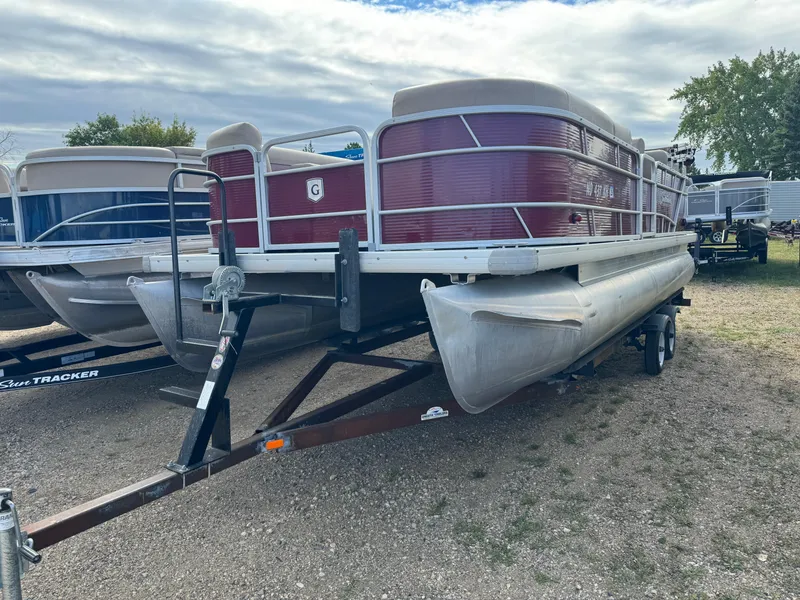 Slide: The Image of 2016 Godfrey Sweet Water pontoon boat on trailer, parked on gravel lot under cloudy sky. - 1