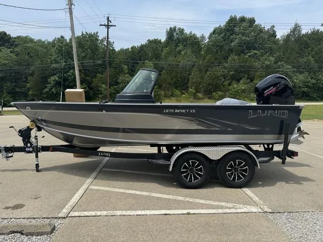 Slide: The Image of 2024 Lund 1875 Impact XS Sport fishing boat on trailer in parking lot. - 13