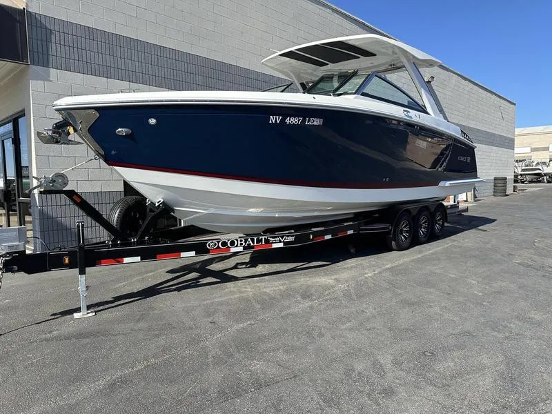 Slide: The Image of 2023 Cobalt R33 boat on trailer, parked outdoors, blue and white design. - 2