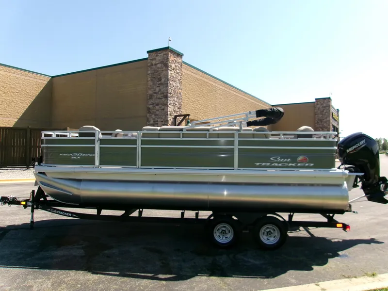 Slide: The Image of 2024 Sun Tracker Fishin' Barge 20 DLX pontoon boat on trailer, parked outdoors. - 2