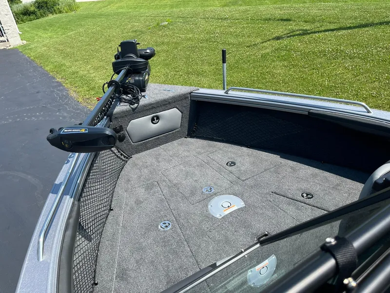 Slide: The Image of 2025 Lund 2275 Baron boat deck with trolling motor, gray carpet, and green grass background. - 20