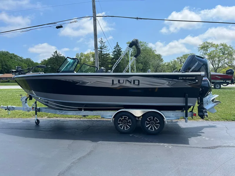 Slide: The Image of 2025 Lund 2275 Baron boat on trailer, parked outdoors under a clear sky. - 4