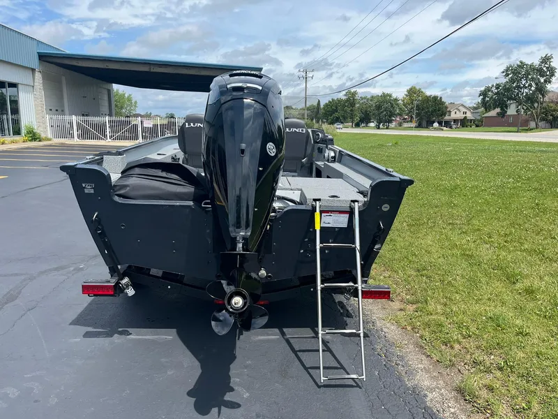 Slide: The Image of 2025 Lund 1775 Adventure SS boat with outboard motor and ladder, parked on pavement. - 2