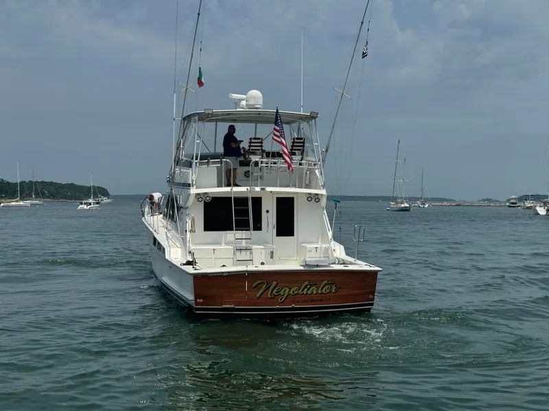 Slide: The Image of 1994 Hatteras 54 Convertible yacht on water, rear view with flags and person onboard. - 2
