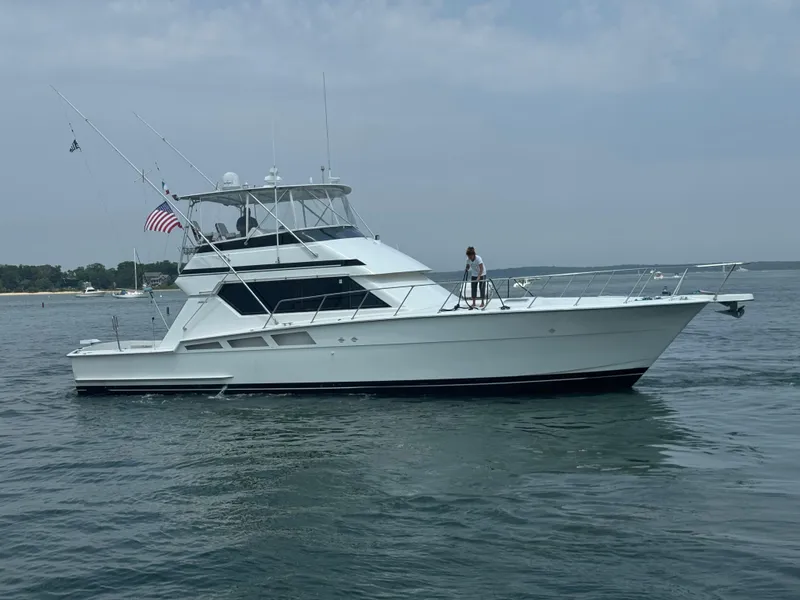 Slide: The Image of 1994 Hatteras 54 Convertible yacht on calm water, featuring fishing rods and an American flag. - 4