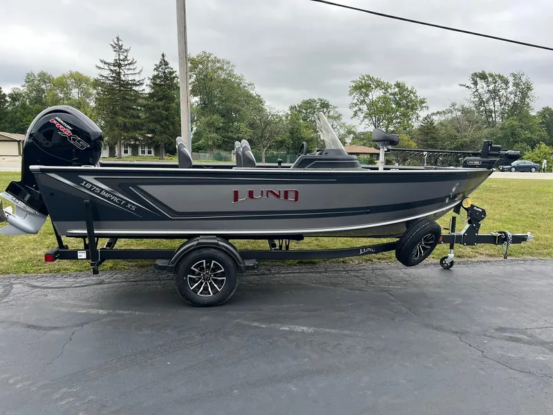 Slide: The Image of 2025 Lund 1875 Impact XS SS fishing boat on trailer, parked outdoors. - 2