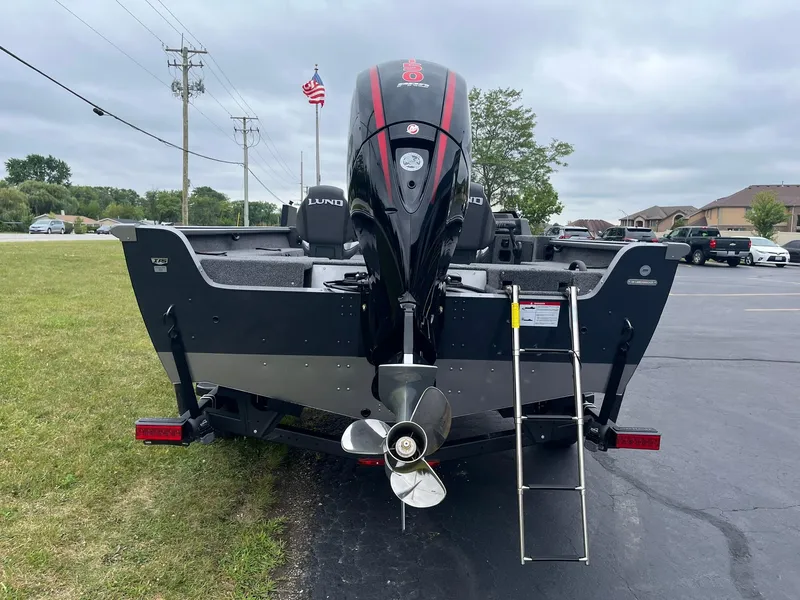 Slide: The Image of 2025 Lund 1875 Impact XS SS boat with outboard motor and ladder, parked on pavement. - 3