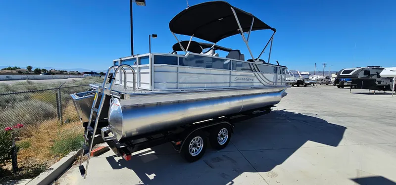 Slide: The Image of 2025 South Bay 224FCRLE pontoon boat on a trailer in a parking lot. - 1