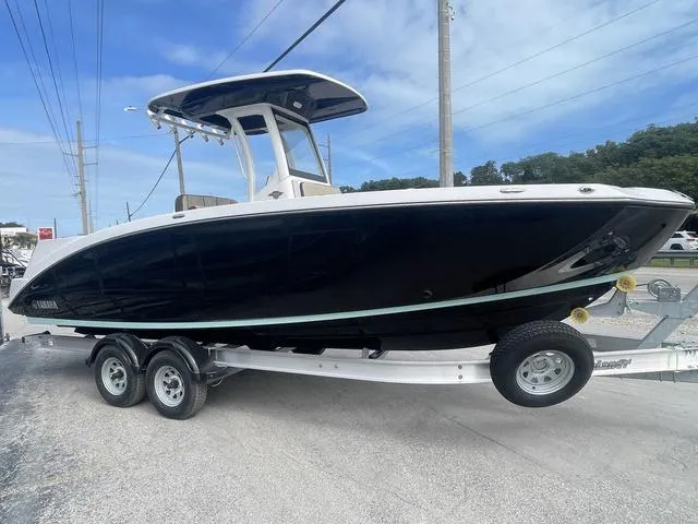 Slide: The Image of 2024 Yamaha Boats 252 FSH Sport on trailer, black hull, blue sky background. - 3
