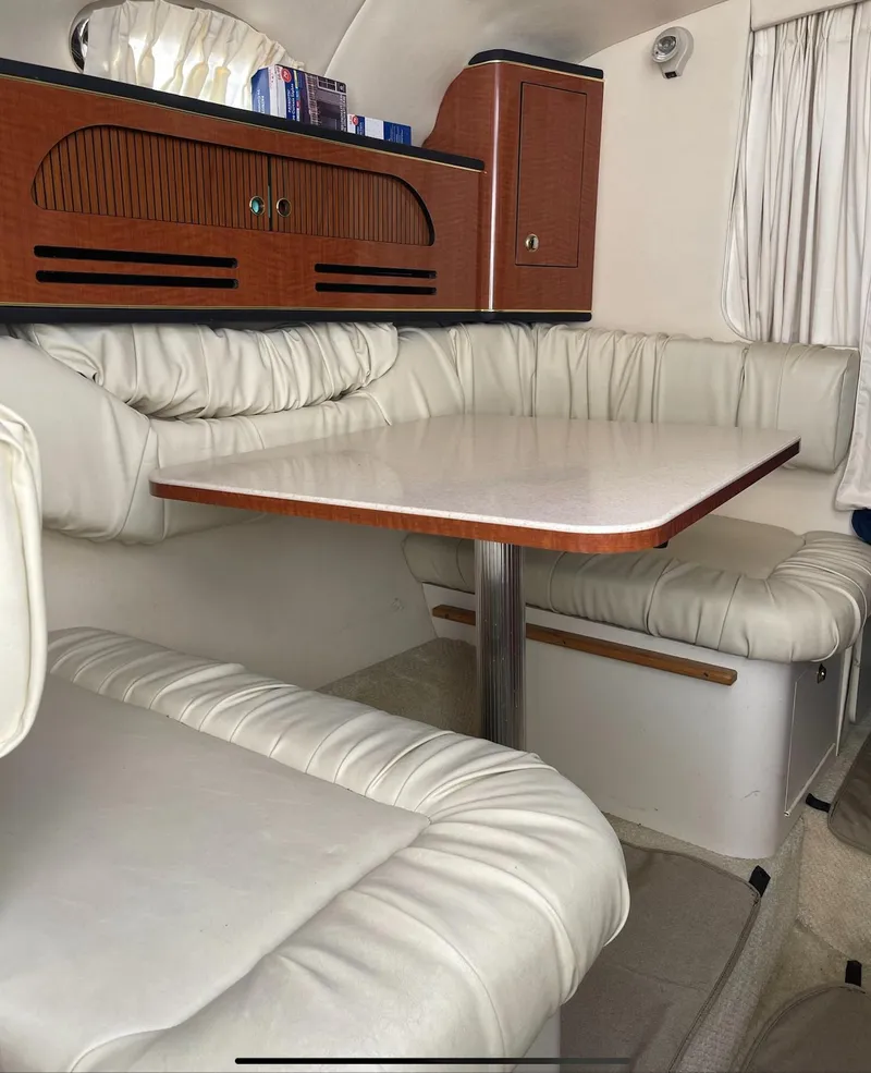 Slide: The Image of 2002 Sea Ray 280 Sundancer interior with white leather seating and wooden table. - 13