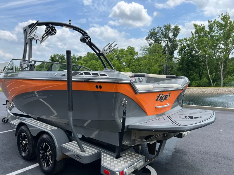 Slide: The Image of 2017 Tigé R21 boat on trailer, orange and gray, parked near water. - 5