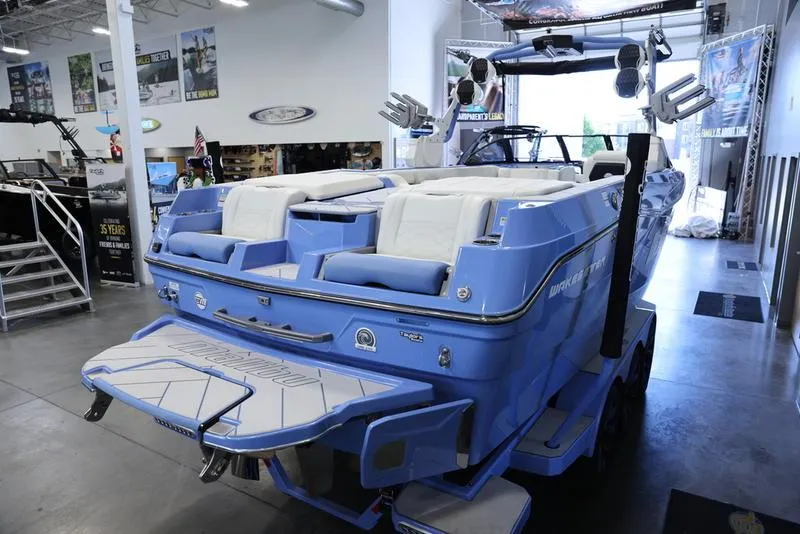 Slide: The Image of 2024 Malibu 26 LSV boat in showroom, rear view with blue and white seating. - 10
