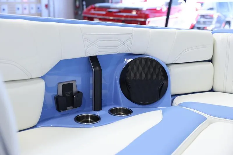 Slide: The Image of 2024 Malibu 26 LSV boat interior with blue and white seating, cup holders, and speaker. - 21