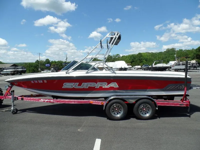 Slide: The Image of 2003 Supra 21 boat on trailer, red and white, parked outdoors. - 2