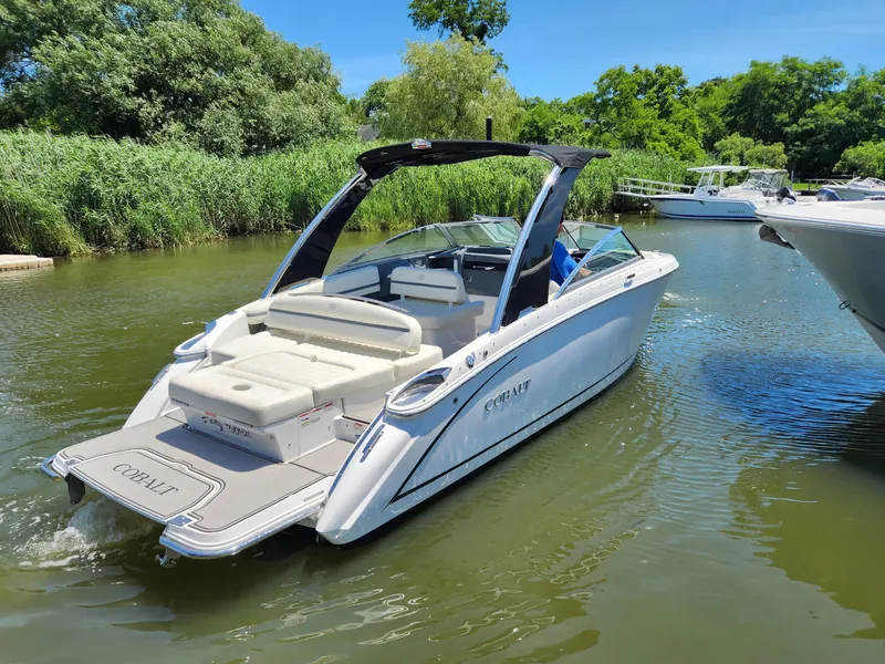 Slide: The Image of 2020 Cobalt R5 boat cruising on a calm river with lush greenery. - 2