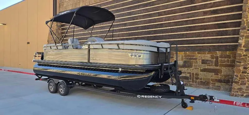 Slide: The Image of 2024 Regency 230 DL3 pontoon boat on trailer, parked outdoors. - 2