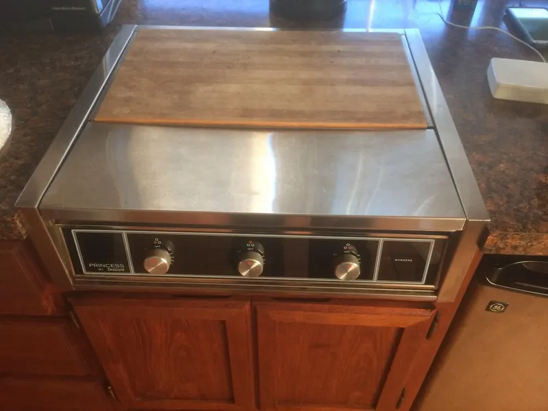 Slide: The Image of Stainless steel stovetop with wooden cutting board, featuring three control knobs. - 24