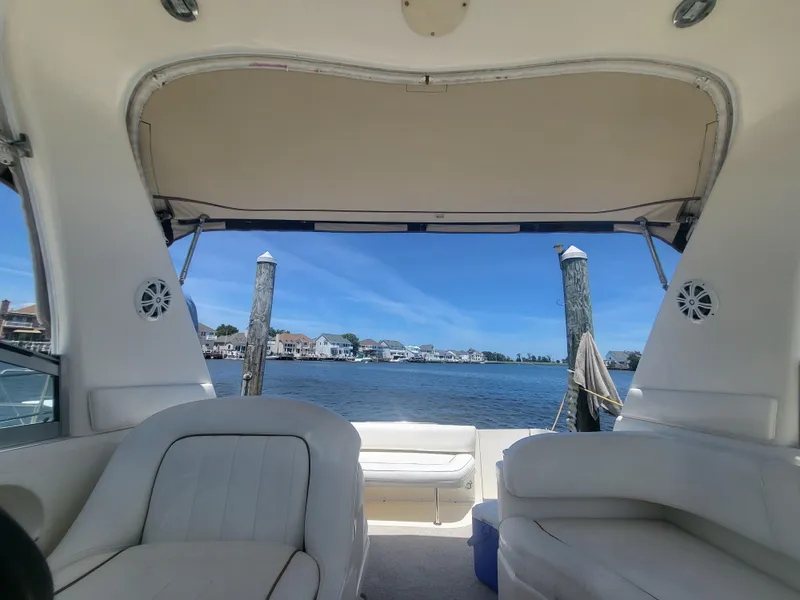Slide: The Image of 1999 Sea Ray 290 Sundancer interior with waterfront view, featuring white seating and open canopy. - 15