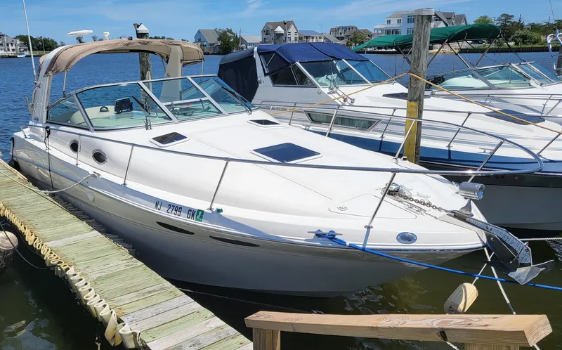 Slide: The Image of 1999 Sea Ray 290 Sundancer docked at a marina, clear sky, waterfront homes in background. - 3