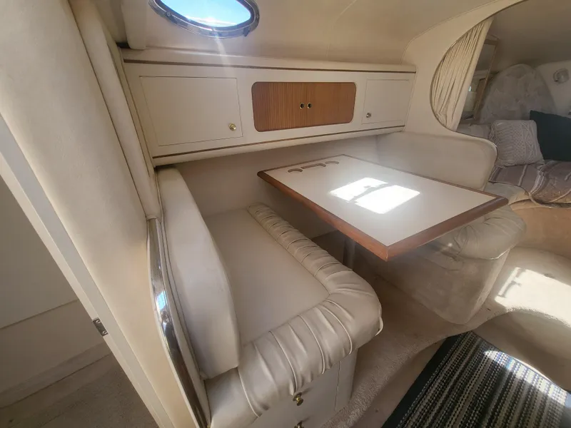 Slide: The Image of 1999 Sea Ray 290 Sundancer cabin with dining area, featuring cushioned seating and a wooden table. - 8
