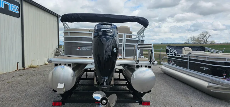 Slide: The Image of 2024 Sun Tracker Party Barge 20 DLX pontoon boat, rear view with motor, parked outdoors. - 2