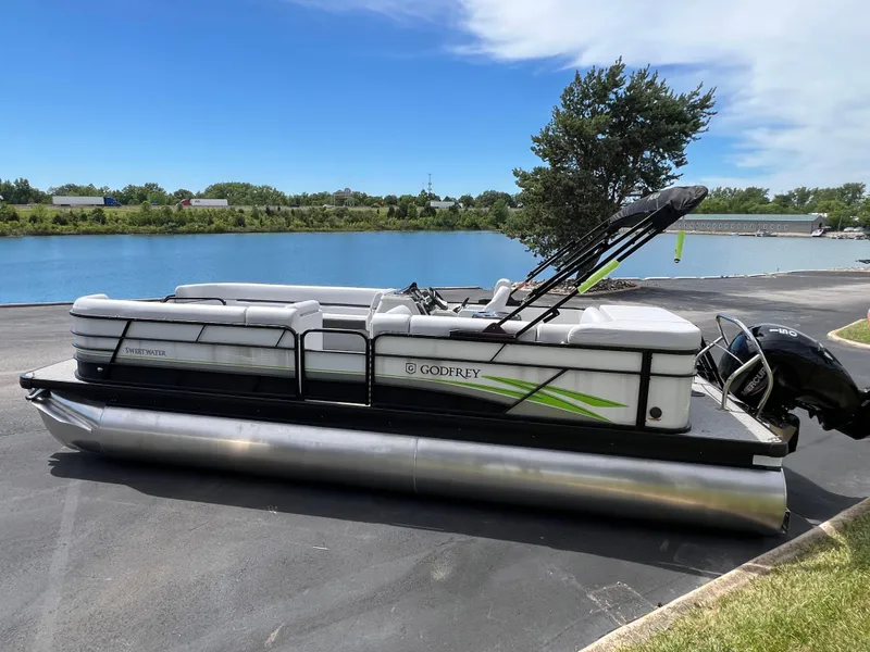 Slide: The Image of 2023 Godfrey Sweetwater 2486 C pontoon boat by a lake on a sunny day. - 1