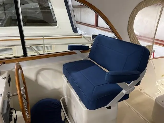Slide: The Image of 2003 Legacy Yachts 34 Sedan helm with blue cushioned seat and wooden steering wheel. - 26
