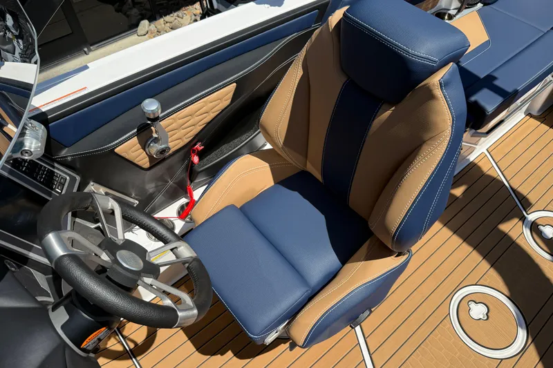 Slide: The Image of 2024 MasterCraft X24 boat interior with blue and tan seating, steering wheel, and teak flooring. - 16