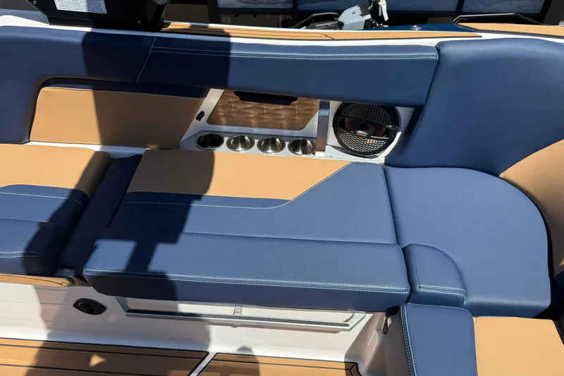 Slide: The Image of 2024 MasterCraft X24 boat interior with blue and tan seating, cup holders, and speaker. - 18