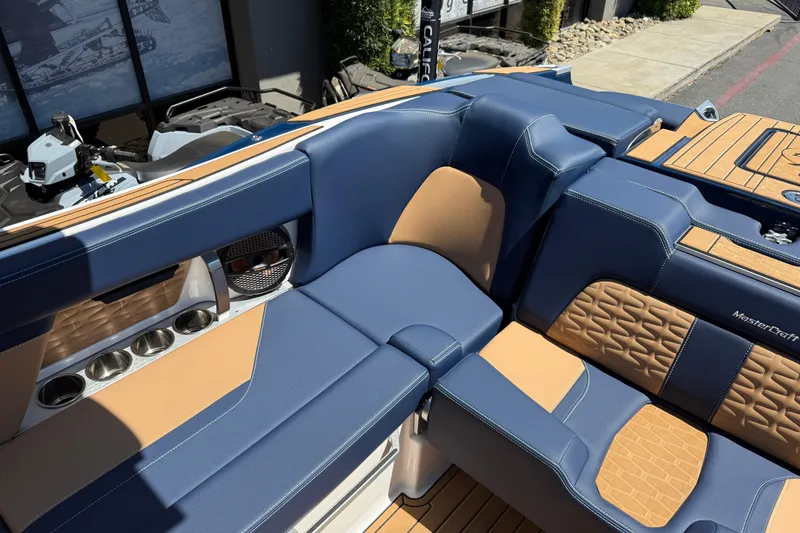 Slide: The Image of 2024 MasterCraft X24 boat interior with blue and tan seating, cup holders, and speaker. - 19